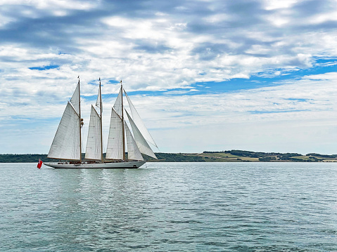 Classic three-masted sailing ship cruising in The Solent, Southern England. Summer in Britain brings out the colours of the countryside and sunlight lifts the hues and shades of the coastal craft and skies in England
