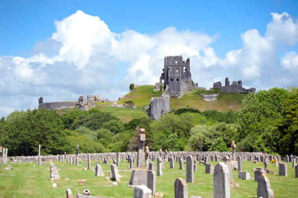Corfe Castle ruins and graveyard scene, Corfe Castle, Dorset, England. Summer in Britain brings out the colours of the countryside and sunlight lifts the hues and shades of natural stone and architecture in the quaint and tranquil villages of England
