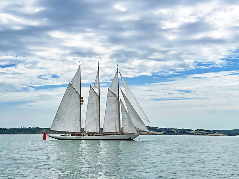 Classic three-masted sailing ship cruising in The Solent, Southern England. Summer in Britain brings out the colours of the countryside and sunlight lifts the hues and shades of the coastal craft and skies in England