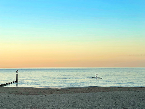 Couple paddle-boarding along Bournemouth beach coastline, England. Summer in Britain brings out the colours of the countryside and sunlight lifts the hues and shades of natural sea landscapes at dusk along the quaint and tranquil shores of England