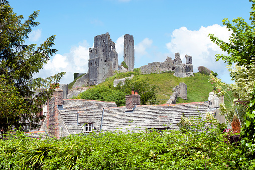 Corfe Castle over rooftops, Corfe Castle, Dorset, England. Summer in Britain brings out the colours of the countryside and sunlight lifts the hues and shades of natural stone and architecture in the quaint and tranquil villages of England