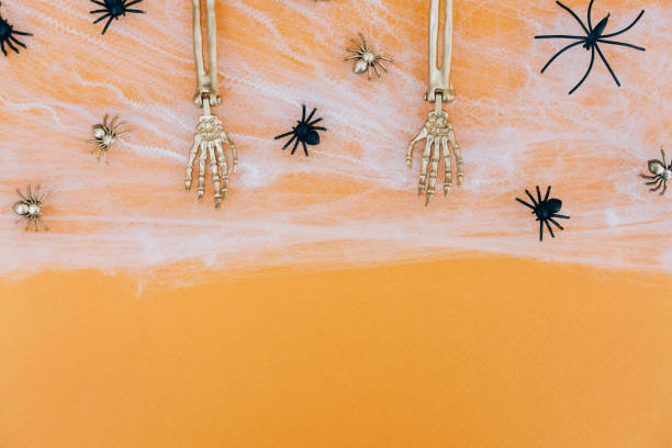 istock Halloween background with cobweb, spiders and golden skeleton hands over orange background with copy space for text. Halloween party invitation template 1411202894