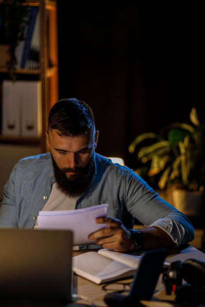 istock Young businessman sitting at his desk late at night and analyzing project documents 1411205614