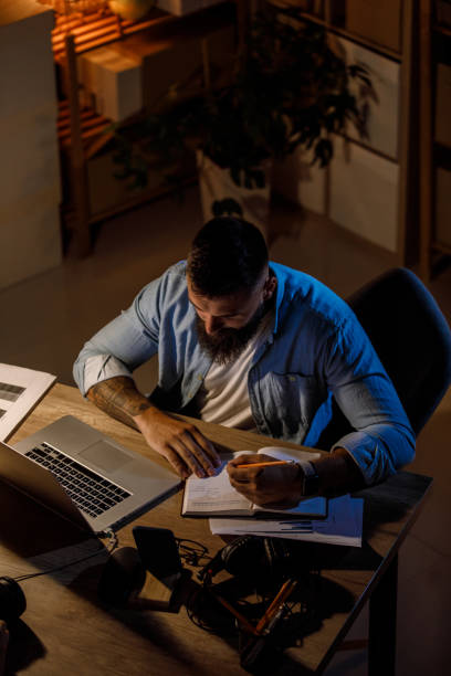 istock Portrait of lefthanded businessman writing notes in a notepad when working late at his desk 1411205620