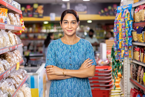 Happy woman owner with arms crossed at grocery aisle of supermarket