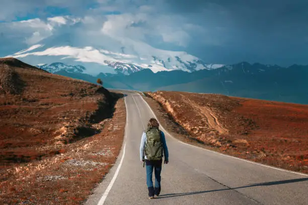 Man traveler with backpack walks along the road in the mountains. View of Elbrus mount, North Caucasus, Russia
