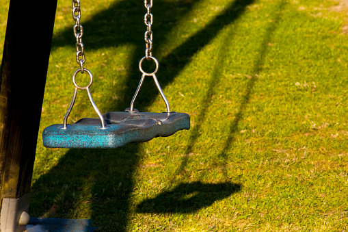 Empty swing and shadow at dusk. children playground. Green grass in the background. Galicia, Spain.