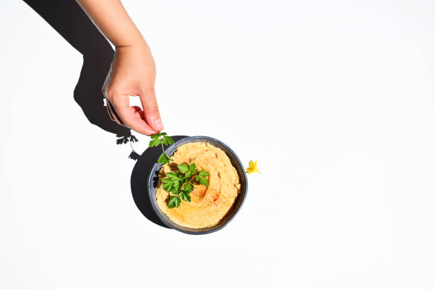Top view of a hand holding parsley next to a bowl with hummus, isolated over white background with copy space for text View from above of a hand holding parsley next to a bowl with hummus, isolated over white background with copy space for text pita bread isolated stock pictures, royalty-free photos & images