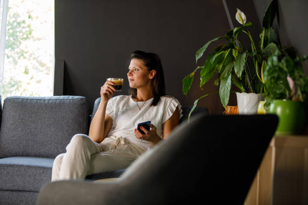 istock Woman sipping coffee, using smart phone and relaxing on the sofa 1411209332