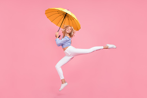Full length photo of dreamy  sweet girl dressed blue top jumping high holding umbrella isolated pink color background.