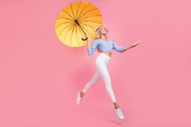 full length photo of pretty dreamy girl dressed blue top jumping high holding umbrella empty space isolated pink color background - rain women umbrella parasol imagens e fotografias de stock