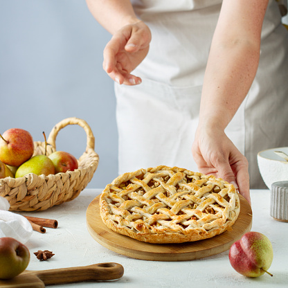 Female hands put a pear pie with a  lattice on the table in the kitchen, ingredients and utensils