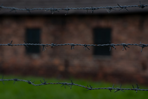 Oswiecim, Poland- 15 August 2022:The path between the barbed wire electrical fences, prisoners barracs and the guard's watch tower in background, Auschwitz concentration camp.