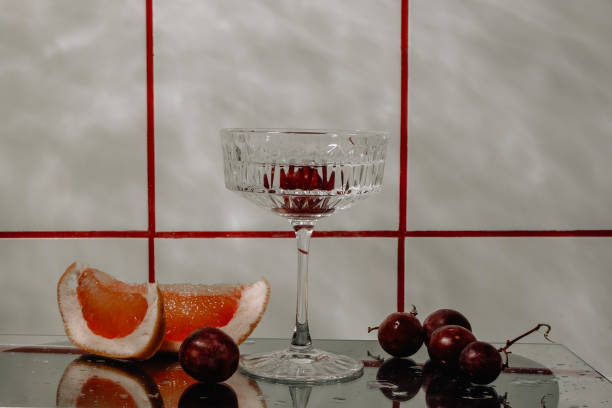 vaso de cristal para cócteles sobre una superficie de cristal. frutas - uvas, pomelo al lado de la copa. antecedentes abstractos. - barware fotografías e imágenes de stock
