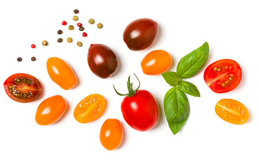 various colorful tomatoes and basil leaves isolated over white background. Top view, flat lay. Creative layout.
