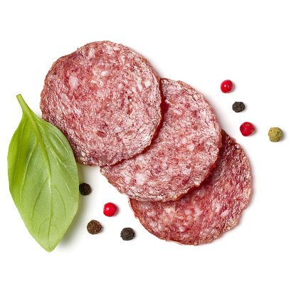 Slices of salami isolated over white background closeup. Sausage and basil leaves top view.