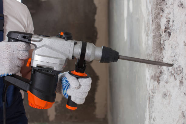 The builder is making hole in wall at construction site with hammer drill perforator equipment. stock photo