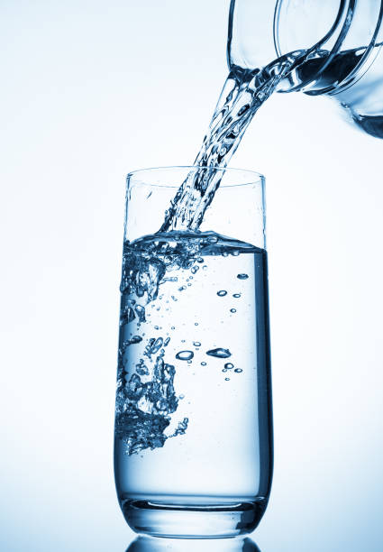 Pouring water from glass pitcher over blue background .