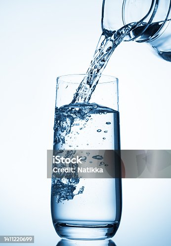 istock Pouring water from glass pitcher over blue background . 1411220699