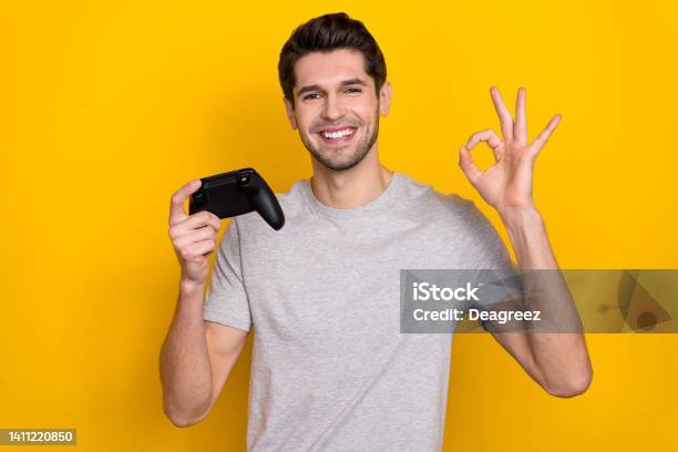 Photo Of Funny Brunet Millennial Guy Playstation Show Okey Wear Grey Tshirt Isolated On Yellow Color Background Stock Photo - Download Image Now