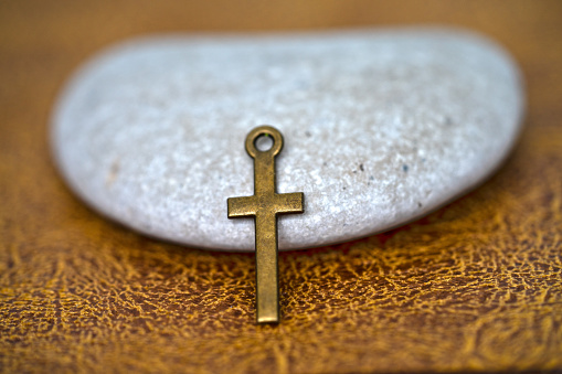 metal cross pandant on the grey pebble with brown leather background for communion to jesus and inspiration