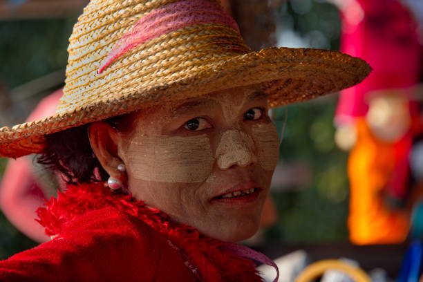 Mandalay. Myanmar. November 21, 2016. A woman in red clothes and a straw hat rests on the bench of the U-Bein Bridge across Lake Taungtaman. A woman's face is usually painted with Tanaka tree paint.