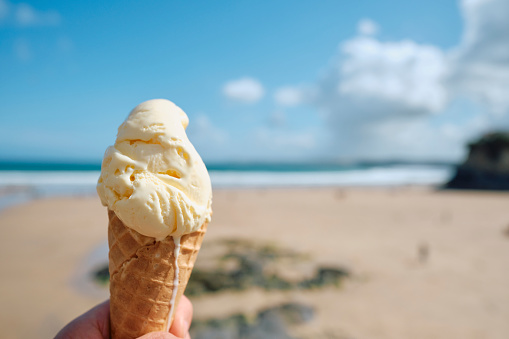 POV of a hand holding a Vanilla Ice Cream cone at Towan Beach, Newquay, Cornwall on a bright sunny June day.