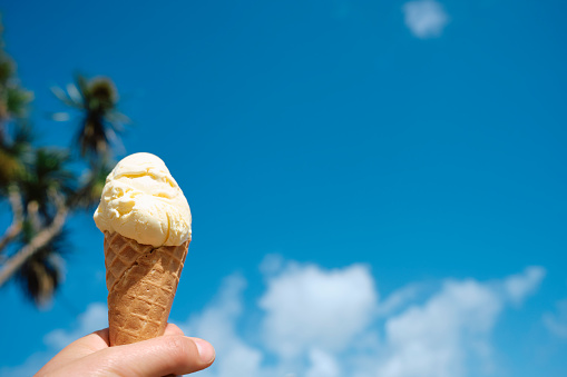 POV of a hand holding a Vanilla Ice Cream cone against a clear blue sky at Newquay, Cornwall on a bright sunny June day.