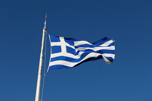 A Greek flag waving in the wind somewhere in Athens with blue and white stripes and cross with the blue sky in the background