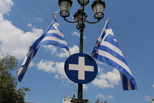 Two Greek flags waving in the wind somewhere in Athens with blue and white stripes and cross with the blue sky in the background