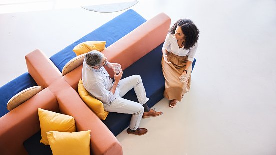 High angle view of two businesspeople talking together in the lounge area of an office during a break