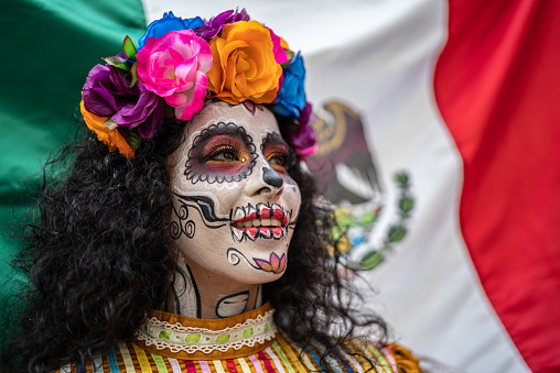 Mid adult woman with makeup of day of the dead and mexican flag