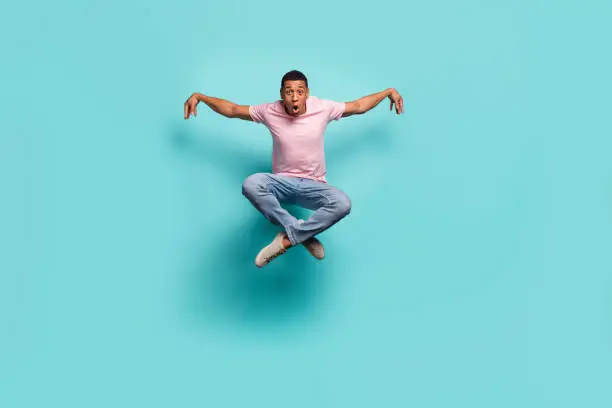 Full length photo of funky cool man dressed pink t-shirt practicing karate jumping high isolated turquoise color background.