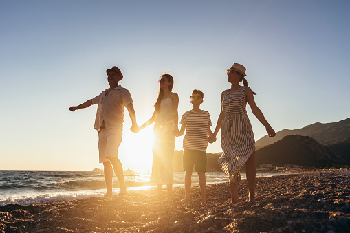 Family holding hands enjoying the sunset on the beach. Happy family travel and vacations concept.