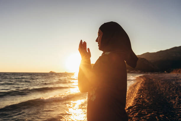 istock Muslim woman praying at sunset with hands up. 1411237085