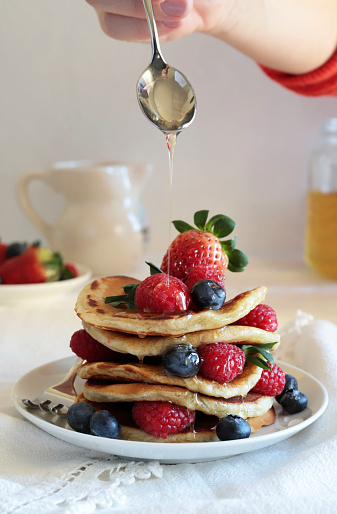 Delicious pancakes with fresh blueberries, raspberries and honey on table. White background.