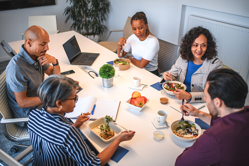 High angle view of multiracial marketing team having vegan food. Five colleagues eating and talking indoors.