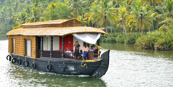 A houseboat with passengers cruises past a lush island in the backwaters of Kerala