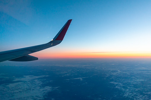 Airplane flight at sunset or dawn. Aircraft's wing and land seen through the illuminator. View from the window of the plane. Airplane, Aircraft. Traveling by air.