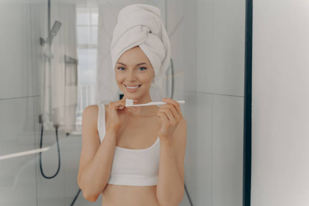 istock Happy beautiful lady with healthy perfect smile brushing teeth while standing in bathroom 1411245594