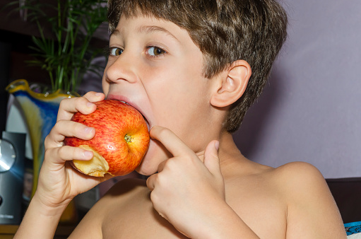 Child eating red apple at home. Salvador, Bahia, Brazil.
