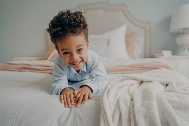 istock Happy curly afro american boy laying on bed and smiling at camera 1411248348