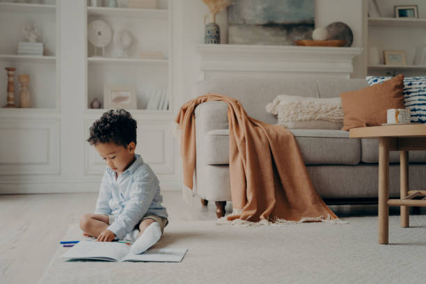 istock African cute boy calmly sitting on warm floor and playing with colored felt tip pens 1411248368