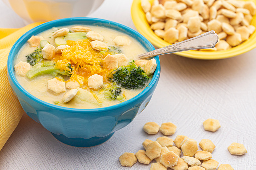 Bowl of Cheddar Cheese and Broccoli Soup with Oyster Crackers on a White Kitchen Counter