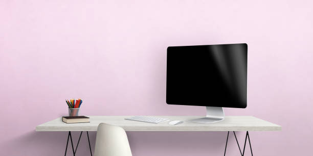 istock Blank computer display on work desk with pens and book beside. Pink wall in background 1411258870