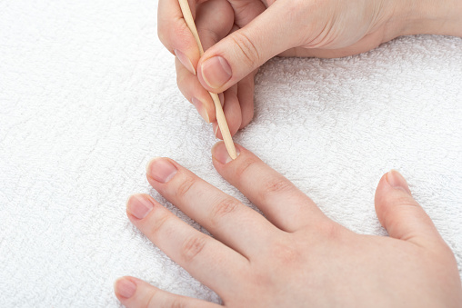 Young woman pushes back the cuticles on her nails with an orange stick. Nail care.