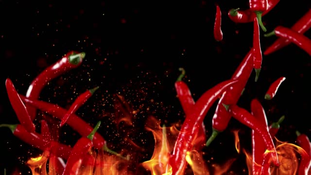 Super slow motion of flying chilli peppers with fire.