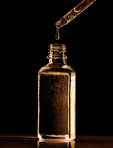 close-up of a serum oil pipette with a falling drop on a dark background