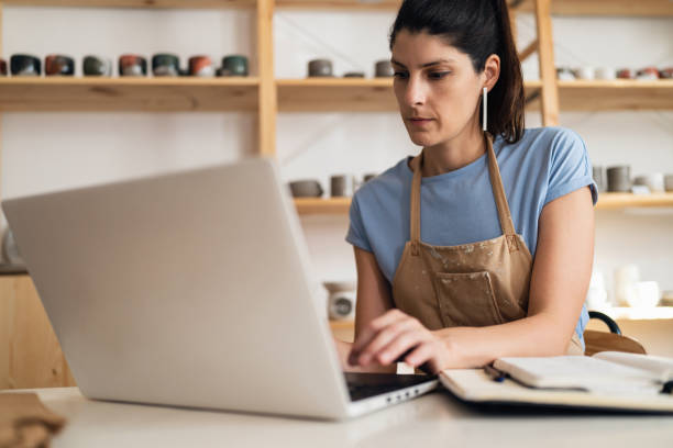 istock Female small business owner working on laptop from her modern pottery studio 1411271719