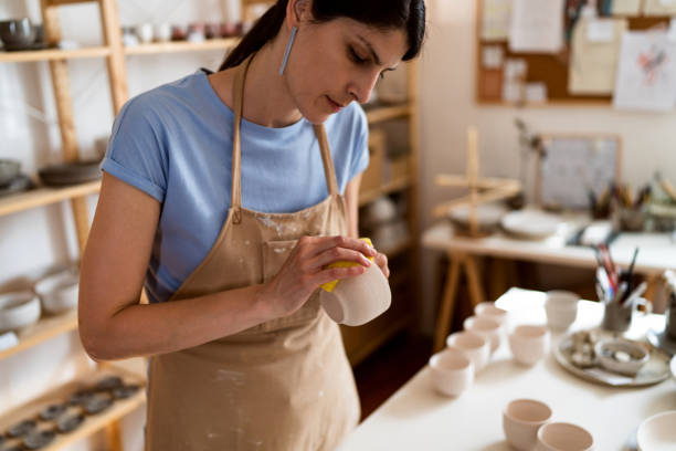 istock Female potter, using sponge to polish the clay cup 1411272357